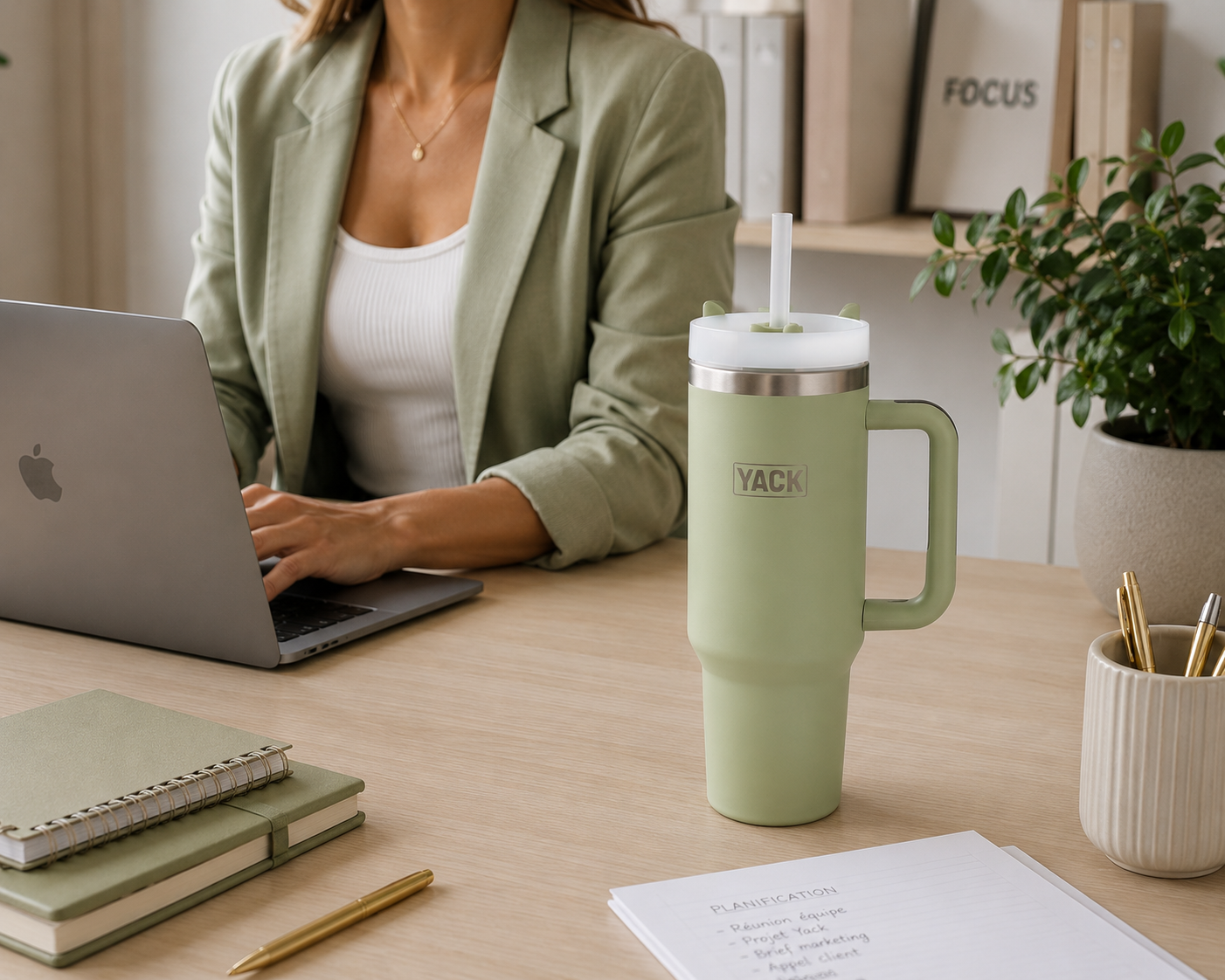 Gobelet isotherme Yack vert 1,2 L avec poignée posé sur un bureau moderne à côté d'une personne travaillant sur un ordinateur portable.